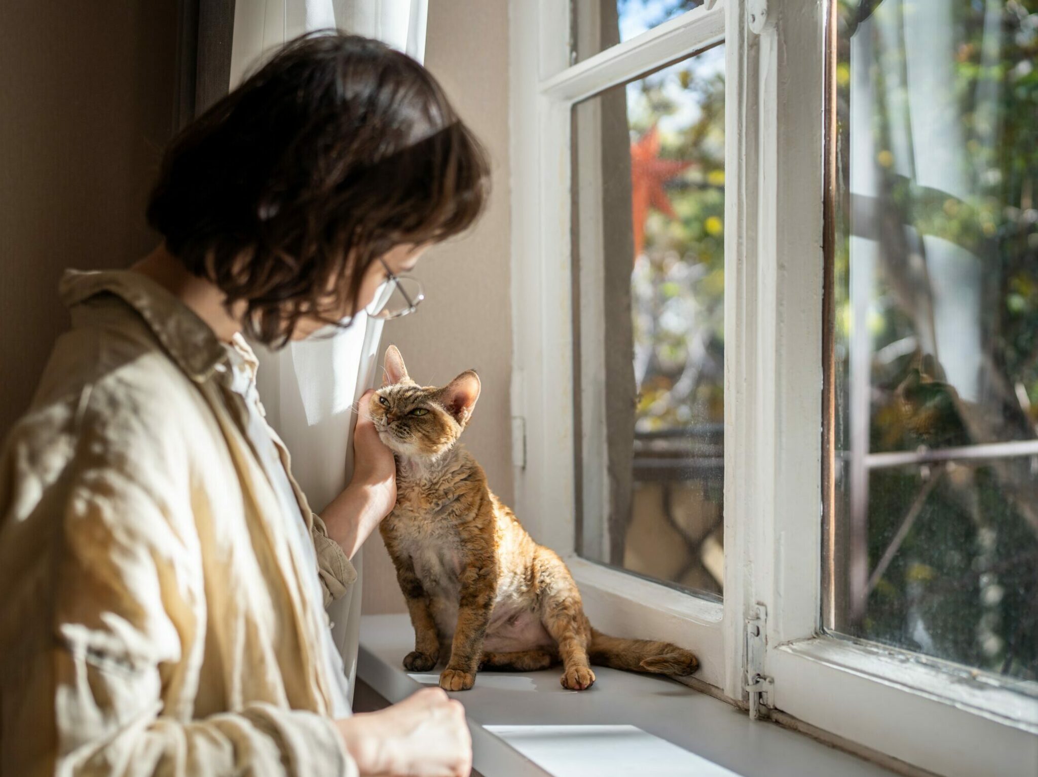 γυναίκα χαϊδεύει τη γάτα της ενώ κάθονται κοντά στο παράθυρο